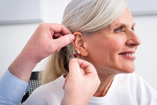 Seniorin bekommt modernes Hörgerät eingesetzt, Hörakustiker unterstützt bei Anpassung.